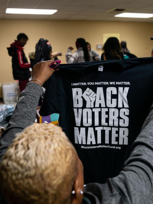 Eine Frau hält ein T-Shirt mit der Aufschrift "Black Voters Matter" in die Höhe.