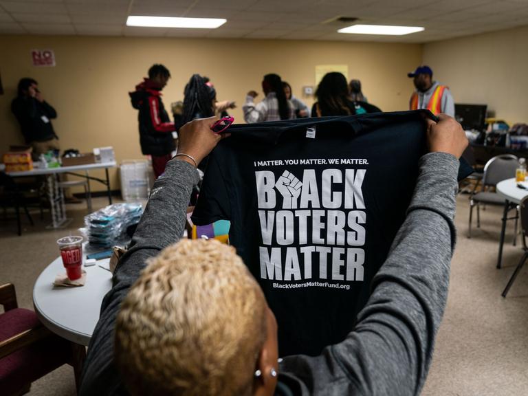 Eine Frau hält ein T-Shirt mit der Aufschrift "Black Voters Matter" in die Höhe.