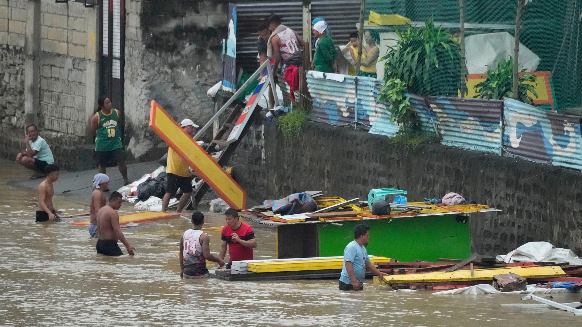 Philippinen, Marikina: Arbeiter transportieren Baumaterialien entlang eines durch die starken Regenfälle des Taifuns "Doksuri"angeschwollenen Flusses.