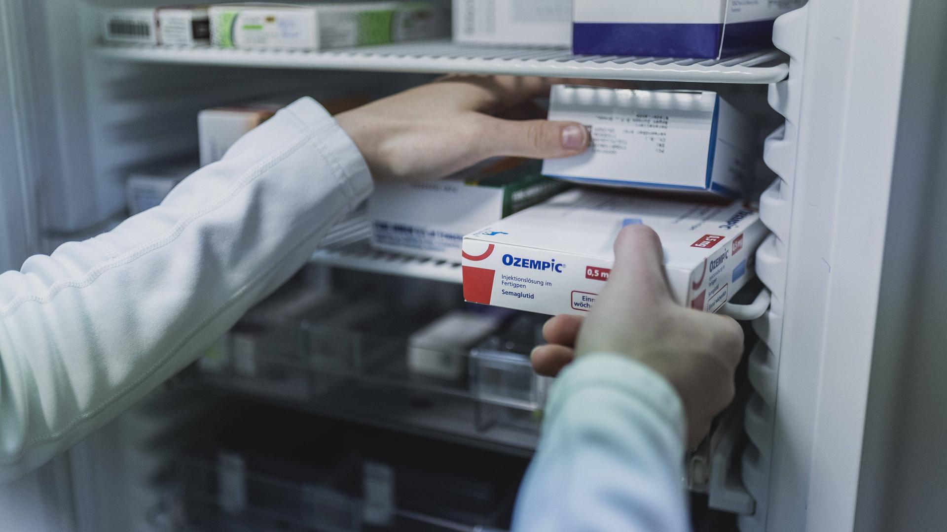 Ein Mensch mit weißem Kittel nimmt in einer Apotheke in Niesky eine Packung Ozempic, ein Antidiabetikum zur Gewichtskontrolle, aus einem Schrank.