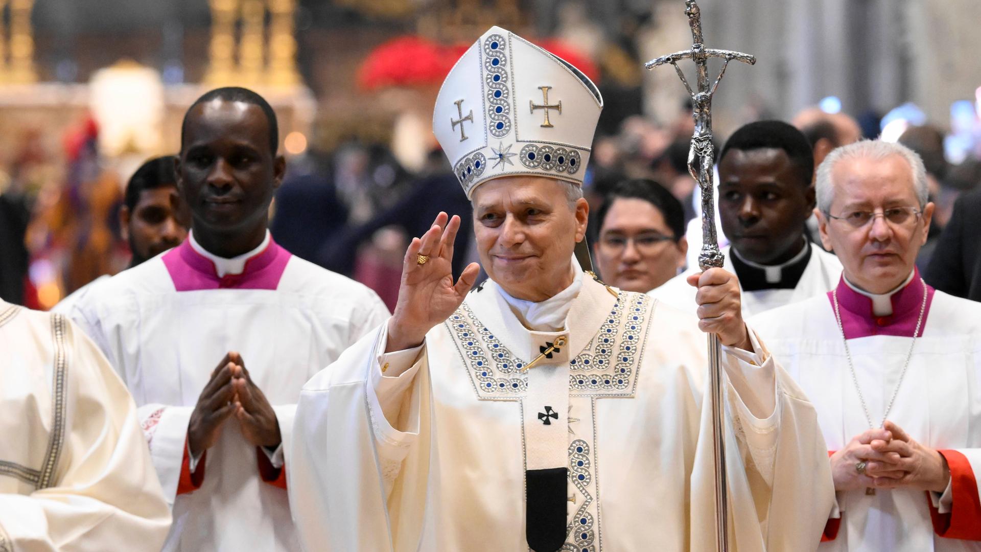 Papst Leo XIV. feiert am Neujahrstag eine Messe in der St.-Peter-Basilika. Er hebt grüßend die Hand. Hinter ihm stehen zwei Bischöfe.