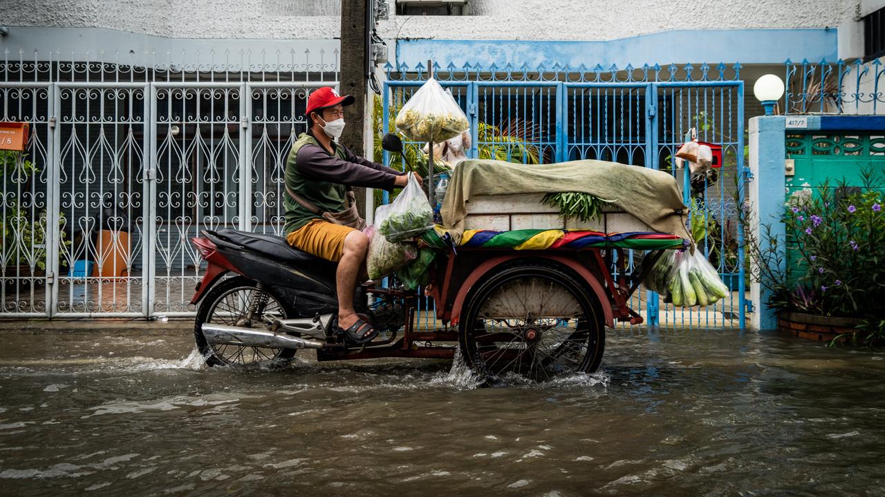 Ein Verkäufer fährt sein mit frischem Gemüse beladenes Motorrad durch eine geflutete Straße.
