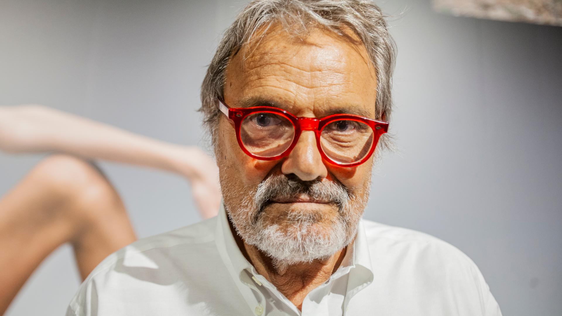 Großaufnahme von Oliviero Toscani, der eine rot gerandete Brille trägt und ernst in die Kamera blickt.