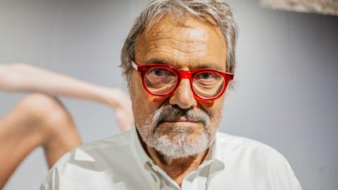 Großaufnahme von Oliviero Toscani, der eine rot gerandete Brille trägt und ernst in die Kamera blickt.