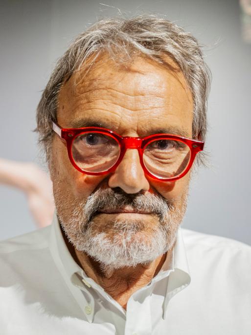 Großaufnahme von Oliviero Toscani, der eine rot gerandete Brille trägt und ernst in die Kamera blickt.