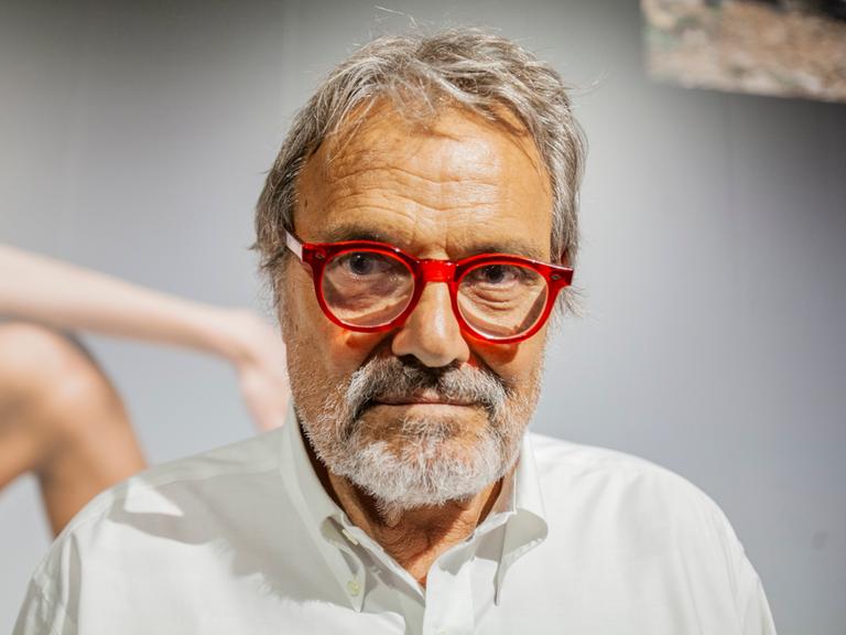 Großaufnahme von Oliviero Toscani, der eine rot gerandete Brille trägt und ernst in die Kamera blickt.