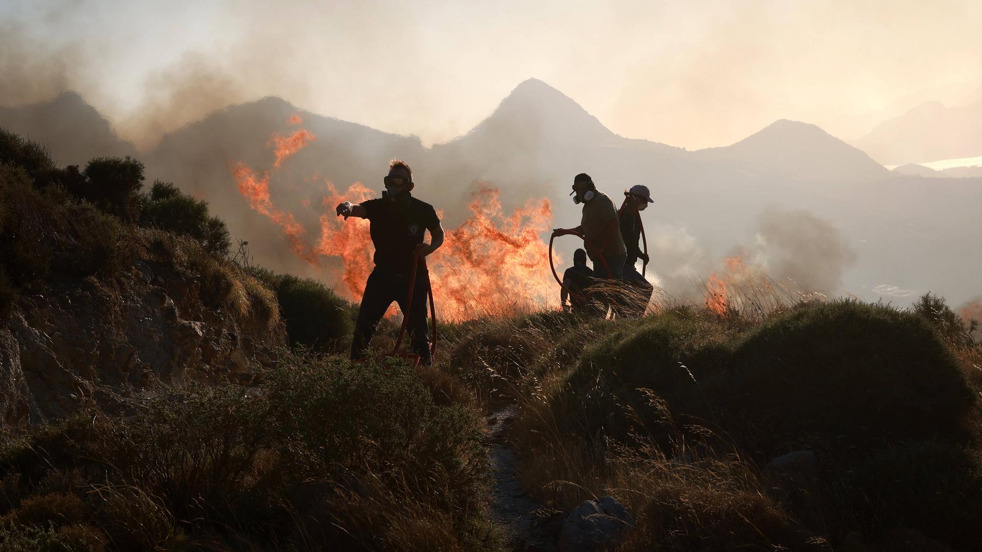 Feuerwehrmänner versuchen brennendes Gebusch in einer hügeligen Umgebung zu löschen. Feuerwehrmänner versuchen brennendes Gebusch in einer hügeligen Umgebung zu löschen.