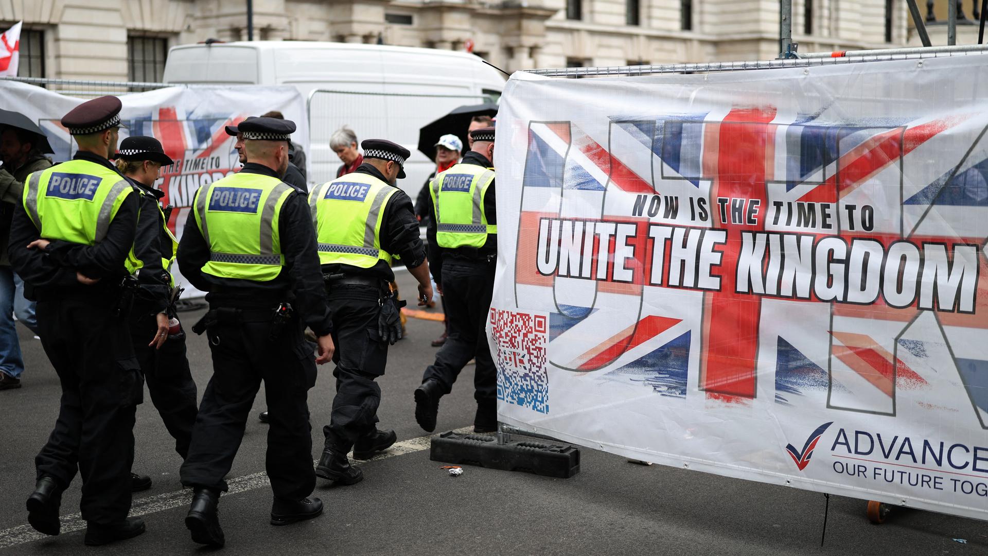 Das Bild zeigt Polizeibeamte auf einer Demonstration in London. Im Bild zu sehen ist die britische Flagge mit der Aufschrift "Unite the Kingdom".