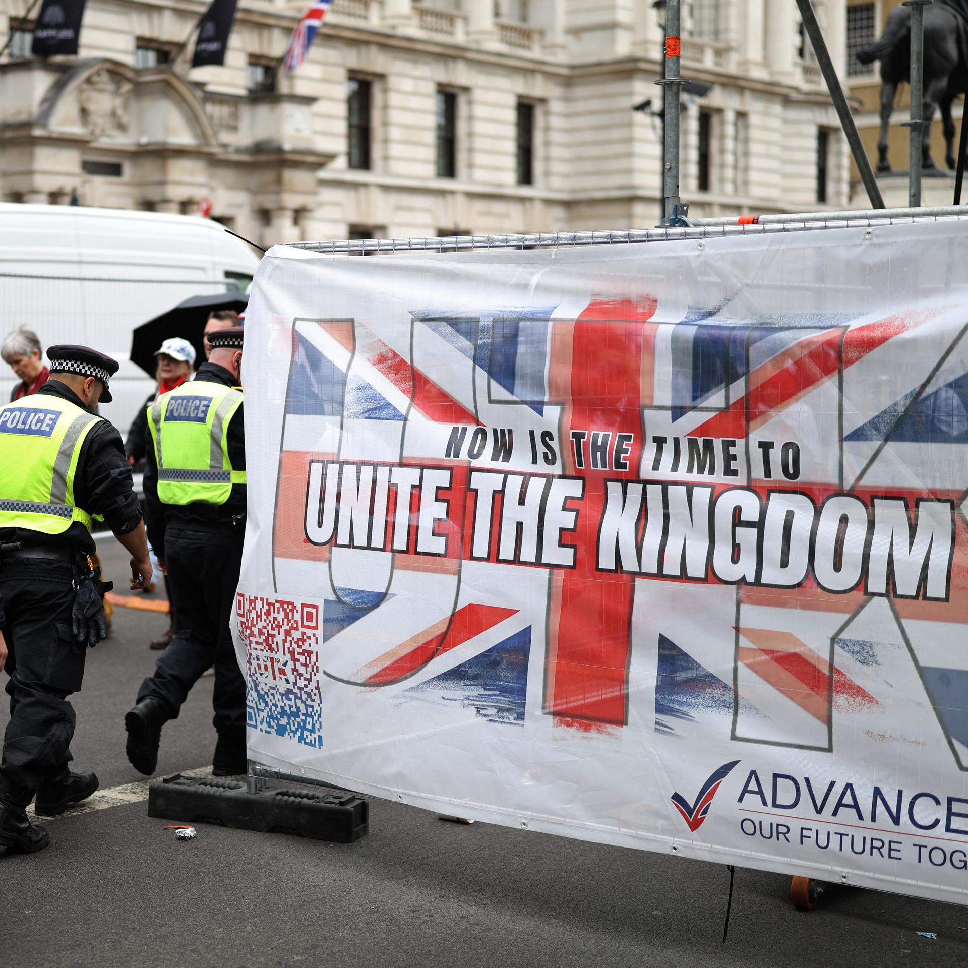 Das Bild zeigt Polizeibeamte auf einer Demonstration in London. Im Bild zu sehen ist die britische Flagge mit der Aufschrift "Unite the Kingdom".