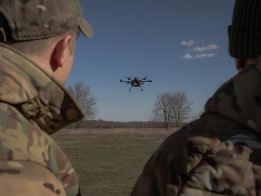 Zwei Militärangehörige beobachten eine Drohne, die über einem Feld aufsteigt.