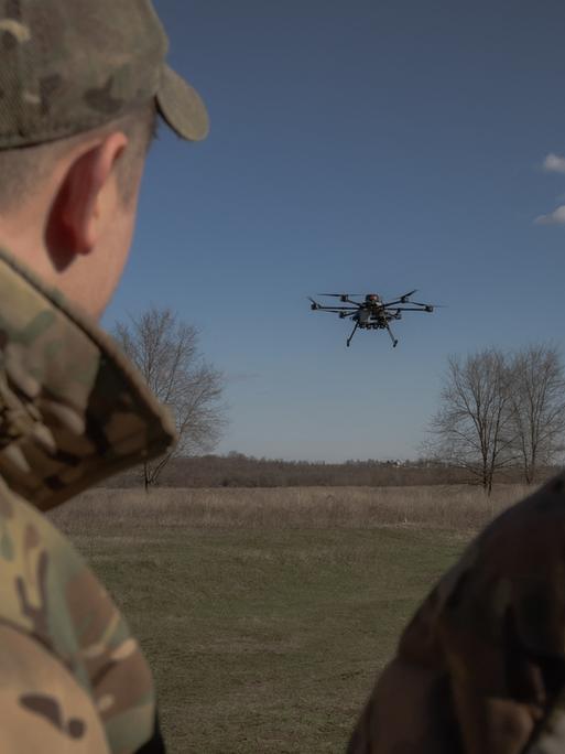 Zwei Militärangehörige beobachten eine Drohne, die über einem Feld aufsteigt.