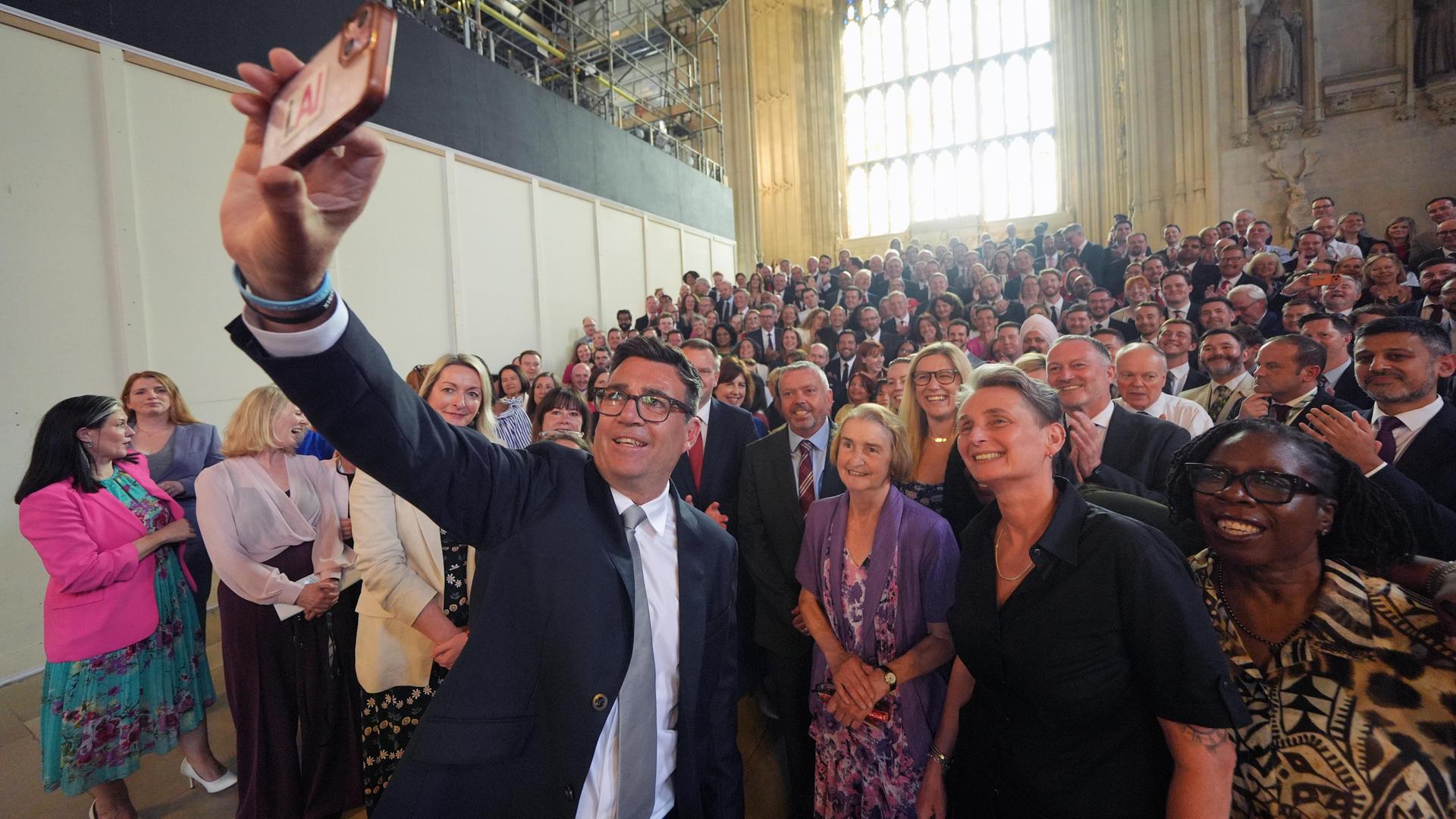 Der Labour-Politiker Andy Burnham macht ein Selfie von sich und zahlreichen Labour-Mitgliedern, die hinter ihm stehen.