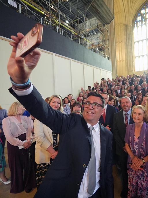 Der Labour-Politiker Andy Burnham macht ein Selfie von sich und zahlreichen Labour-Mitgliedern, die hinter ihm stehen.