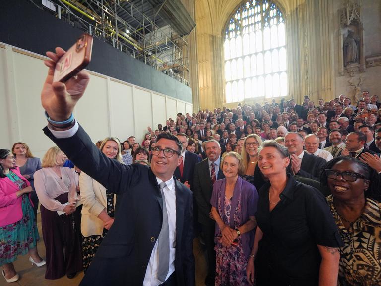 Der Labour-Politiker Andy Burnham macht ein Selfie von sich und zahlreichen Labour-Mitgliedern, die hinter ihm stehen.