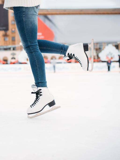 Man sieht die Beine von einem Mann und einer Frau, die auf Schlittschuhen auf dem Eis stehen. 