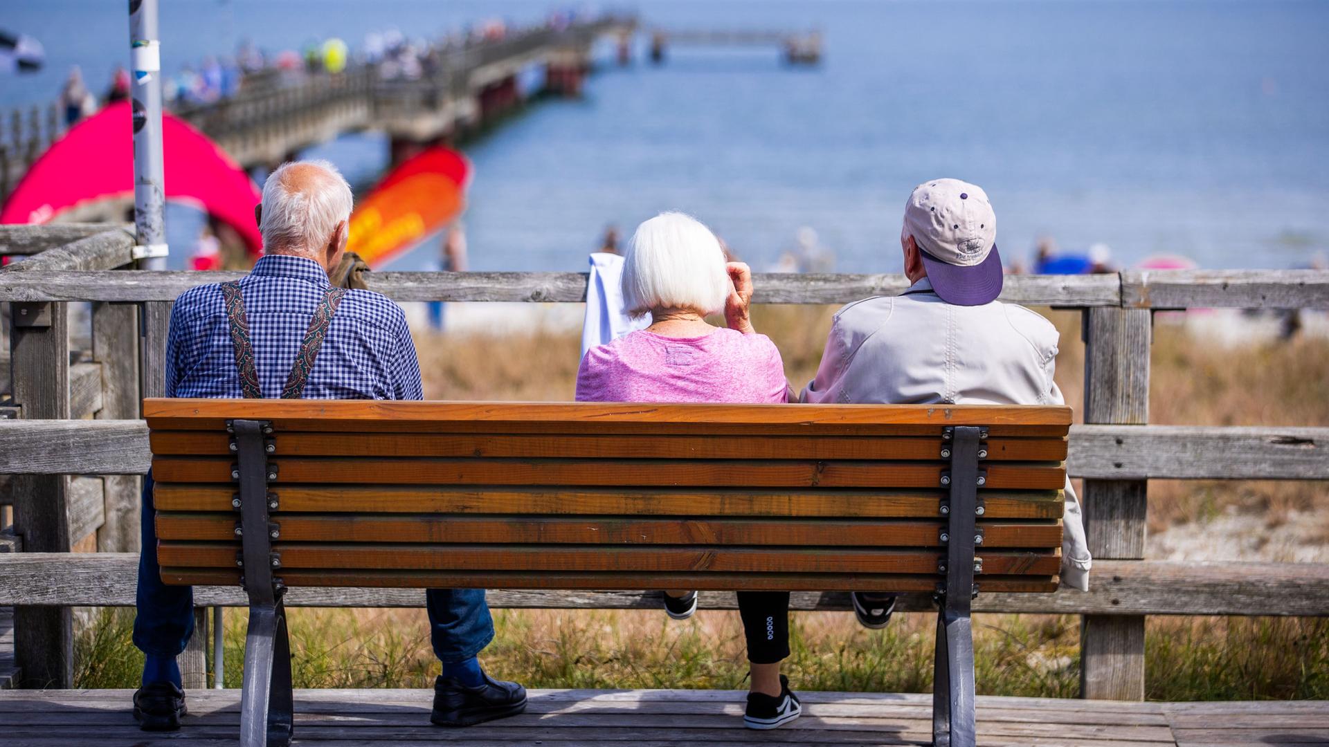 Drei Senioren sitzen auf einer Bank an der Seebrücke.
