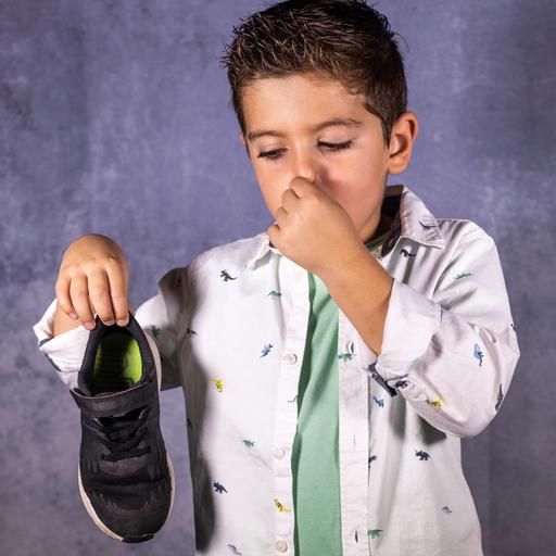 Ein Junge hält einen Turnschuh hoch und sich die Nase zu