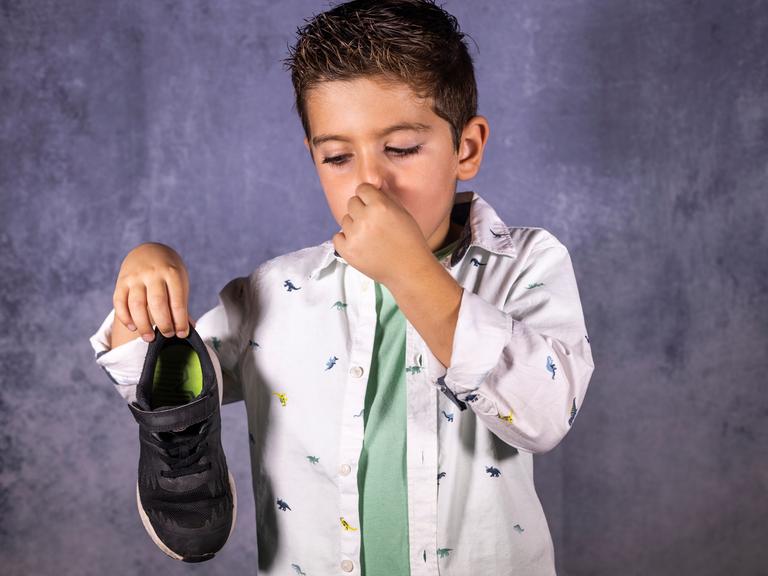 Ein Junge hält einen Turnschuh hoch und sich die Nase zu