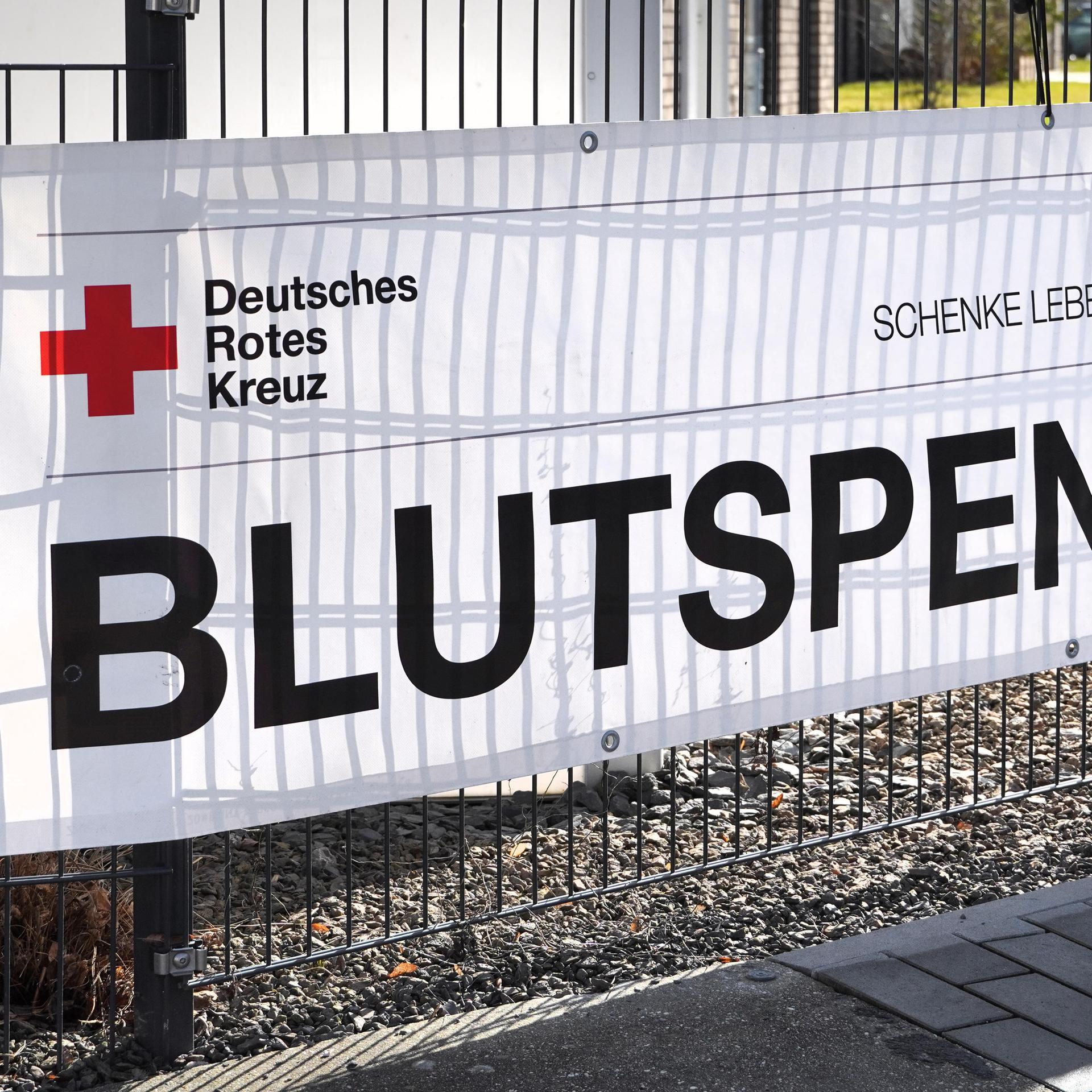 Schrift auf einem Werbebanner an einem Metallzaun: Aufruf des Roten Kreuzes zur Blutspende.