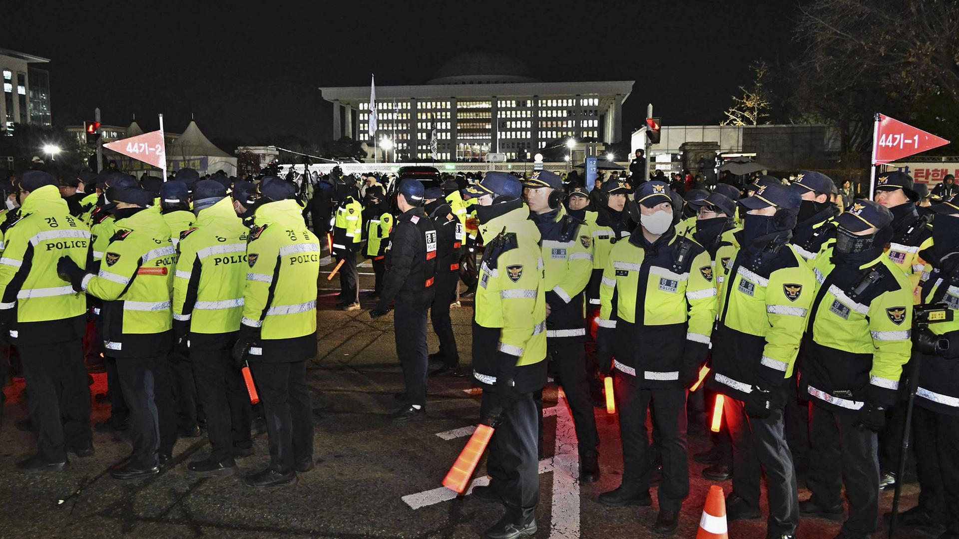 Menschen in Uniform mit neongelben Reflektorelemten auf einem Platz vor einem hell angestrahlten Gebäude.