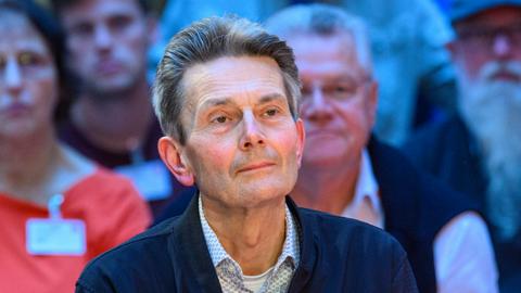 Rolf Mützenich sitzt auf einer Veranstaltung vor mehreren Menschen im Hintergrund.