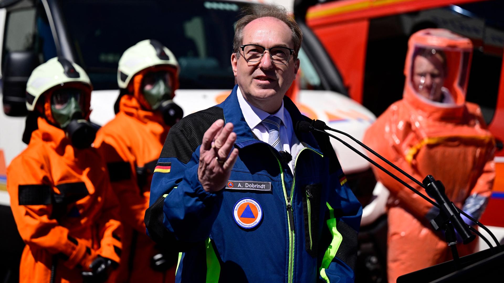 Alexander Dobrindt steht an einem Rednerpult und spricht. Im Hintergrund sind Personen in Schutzkleidung vom THW zu sehen.