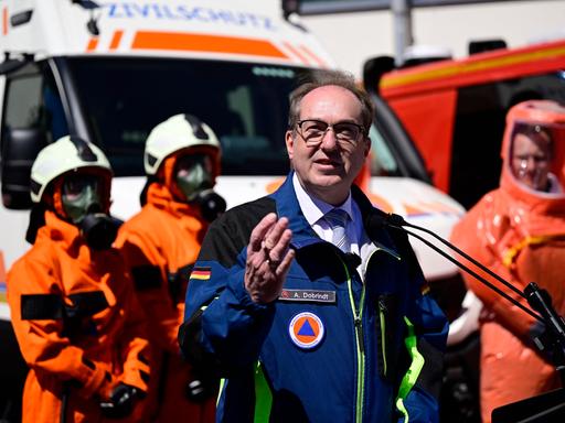 Alexander Dobrindt steht an einem Rednerpult und spricht. Im Hintergrund sind Personen in Schutzkleidung vom THW zu sehen.