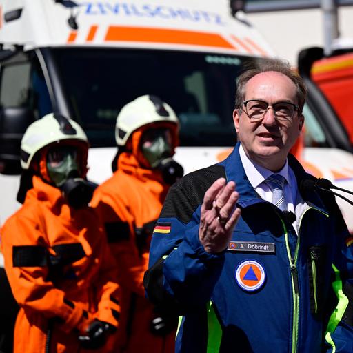 Alexander Dobrindt steht an einem Rednerpult und spricht. Im Hintergrund sind Personen in Schutzkleidung vom THW zu sehen.