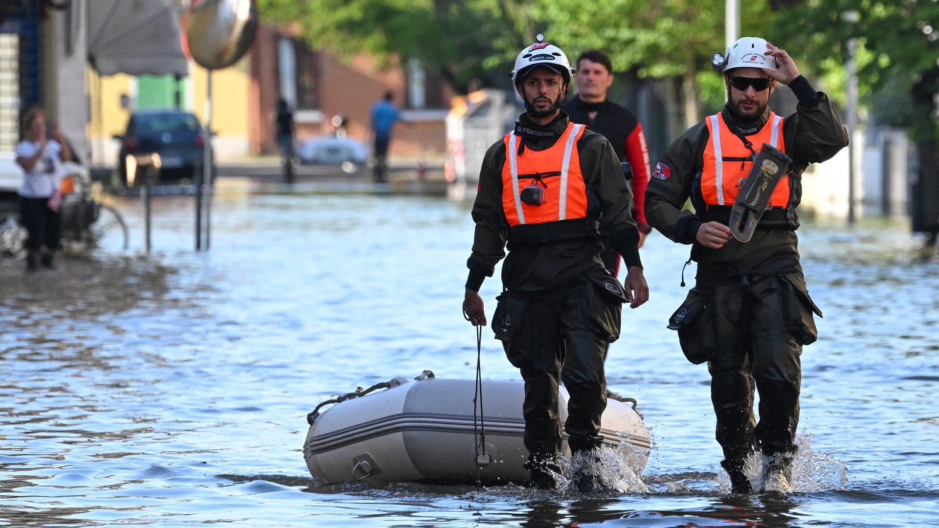 Zwei Männer der italienischen Küstenwache ziehen auf einer überfluteten Straße ein Rettungsboot hinter sich her.