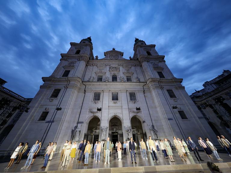 Das Ensemble der Jedermann-Inszenierung steht bei einer Probe auf dem Salzburger Domplatz, dahinter der Dom.