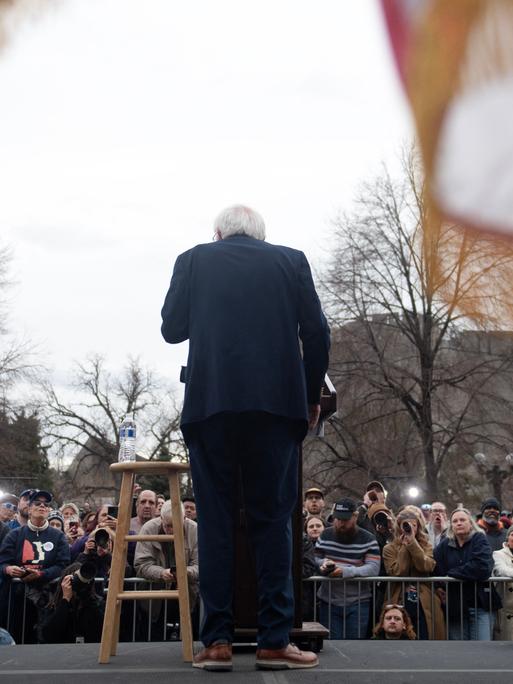 Rückansicht von Bernie Sanders, der während einer Ansprache vor Publikum an einem Pult steht.