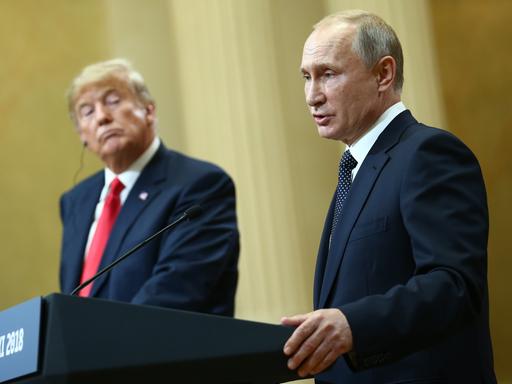 US-Präsident Trump und Russlands Präsident Putin geben gemeinsam eine Pressekonferenz: Putin steht am Redepult und spricht, Trump dreht sich zu ihm und hört zu.