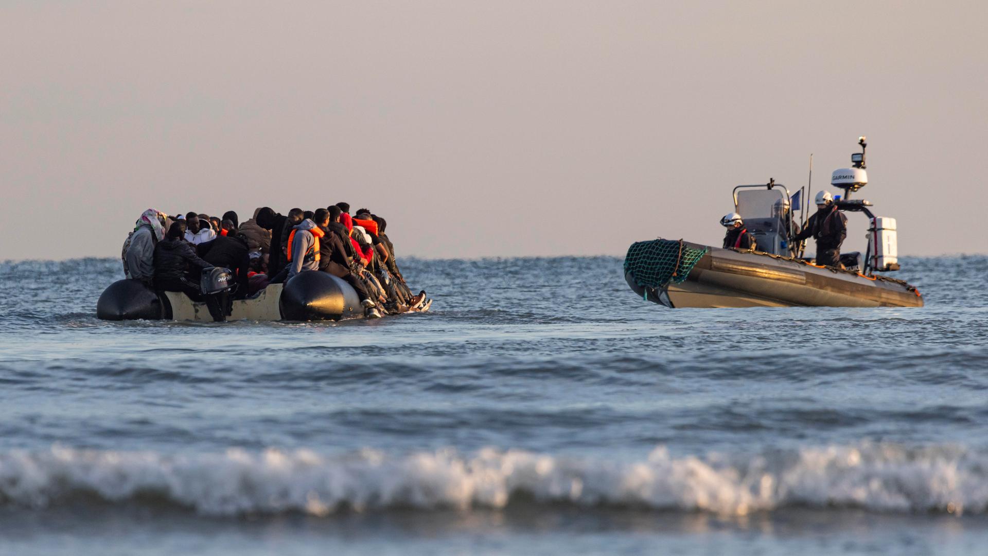 Ein Schlauchboot mit Migranten wird im Wasser von einem Küstenwachschiff beobachtet Ein Schlauchboot mit Migranten wird im Wasser von einem Küstenwachschiff beobachtet