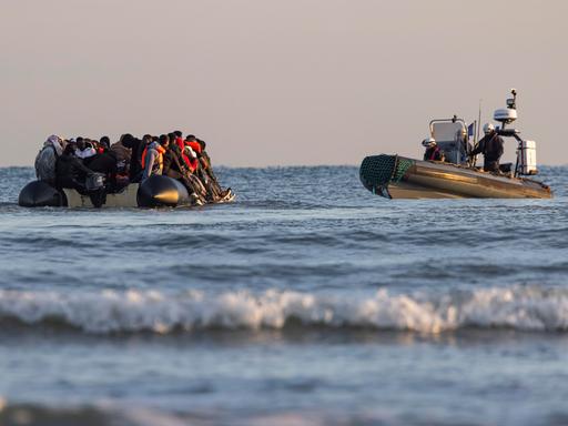 Ein Schlauchboot mit Migranten wird im Wasser von einem Küstenwachschiff beobachtet