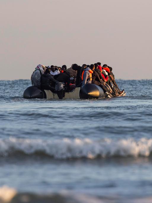 Ein Schlauchboot mit Migranten wird im Wasser von einem Küstenwachschiff beobachtet