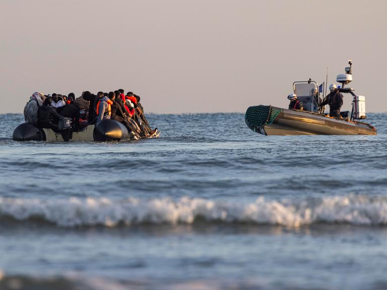 Ein Schlauchboot mit Migranten wird im Wasser von einem Küstenwachschiff beobachtet