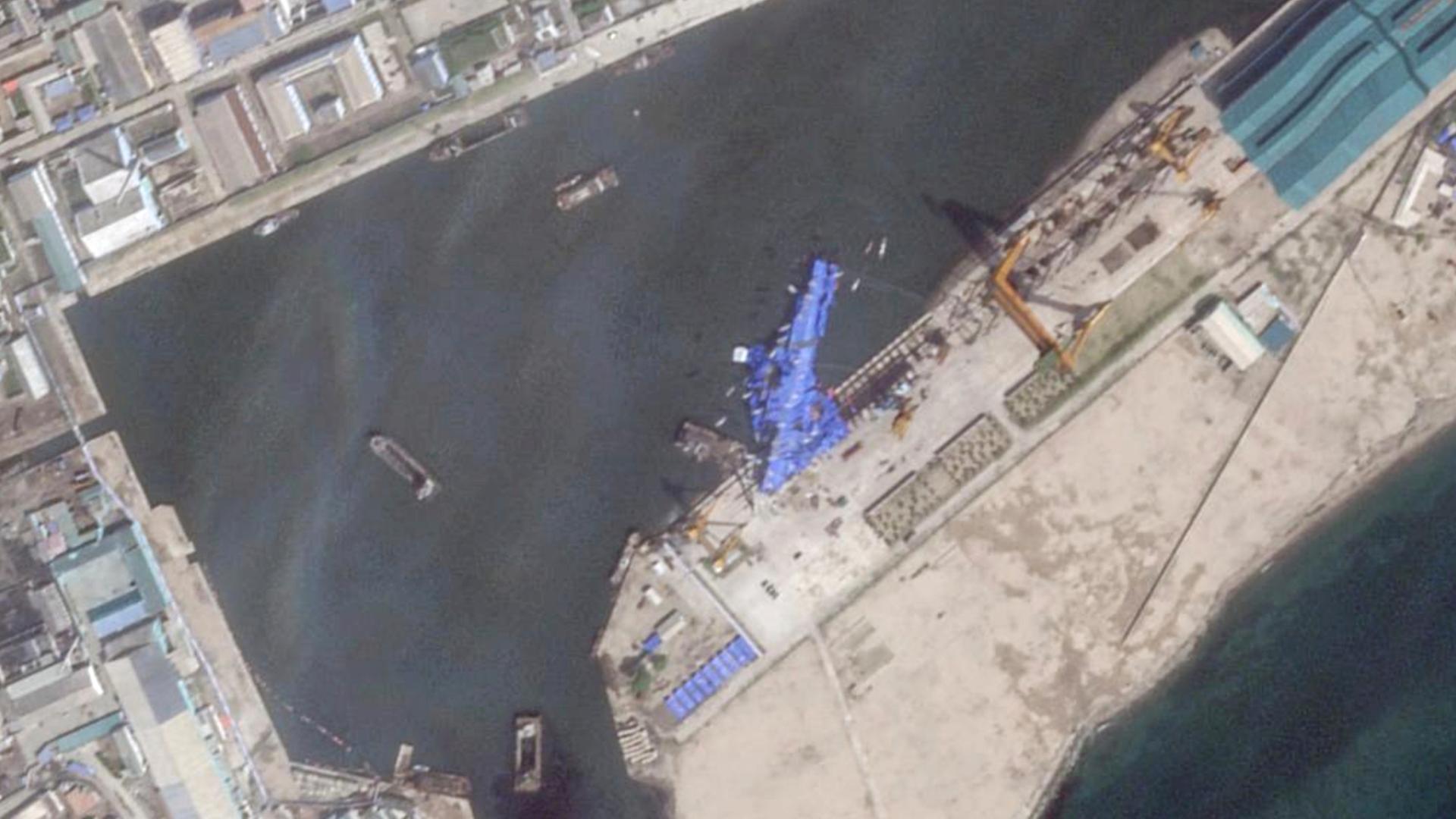 Das Satellitenbild zeigt eine blaue Plane, die einen auf die Seite gekippten nordkoreanischen Zerstörer abdeckt. Unter der Plane zeichnen sich deutlich die Konturen des Kriegsschiffes ab.