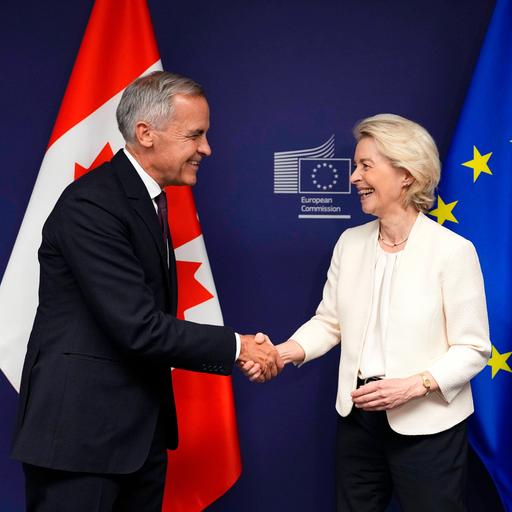 EU-Kommissionspräsidentin Ursula von der Leyen (r.) und er kanadische Premiermininster Mark Carney geben sich lächelnd vor einer kanadischen und einer EU-Fahne die Hand