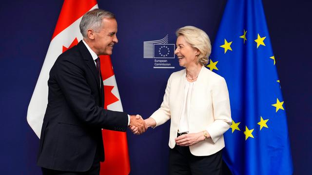 EU-Kommissionspräsidentin Ursula von der Leyen (r.) und er kanadische Premiermininster Mark Carney geben sich lächelnd vor einer kanadischen und einer EU-Fahne die Hand