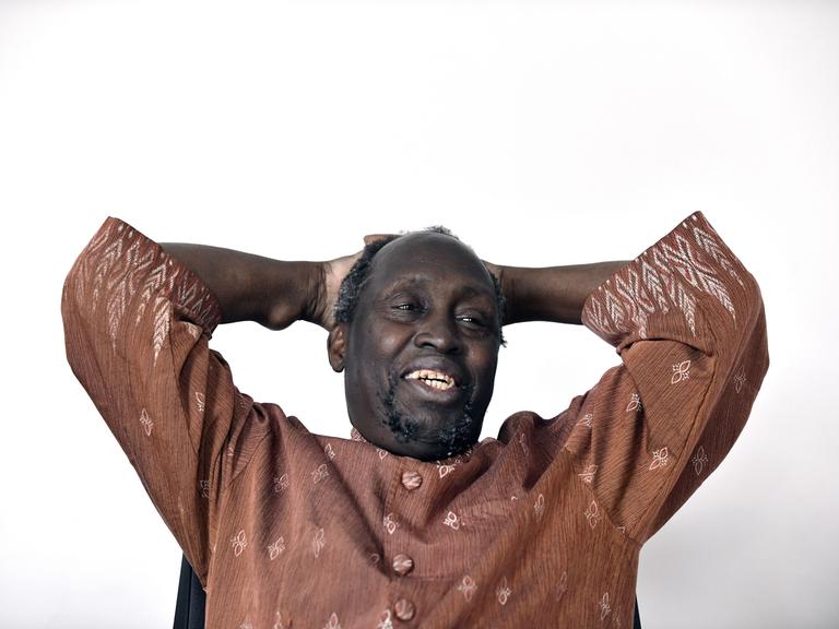 Der kenianische Schriftsteller Ngugi Wa Thiong'o lehnt sich lachend zurück und verschränkt die Hände hinter dem Kopf 