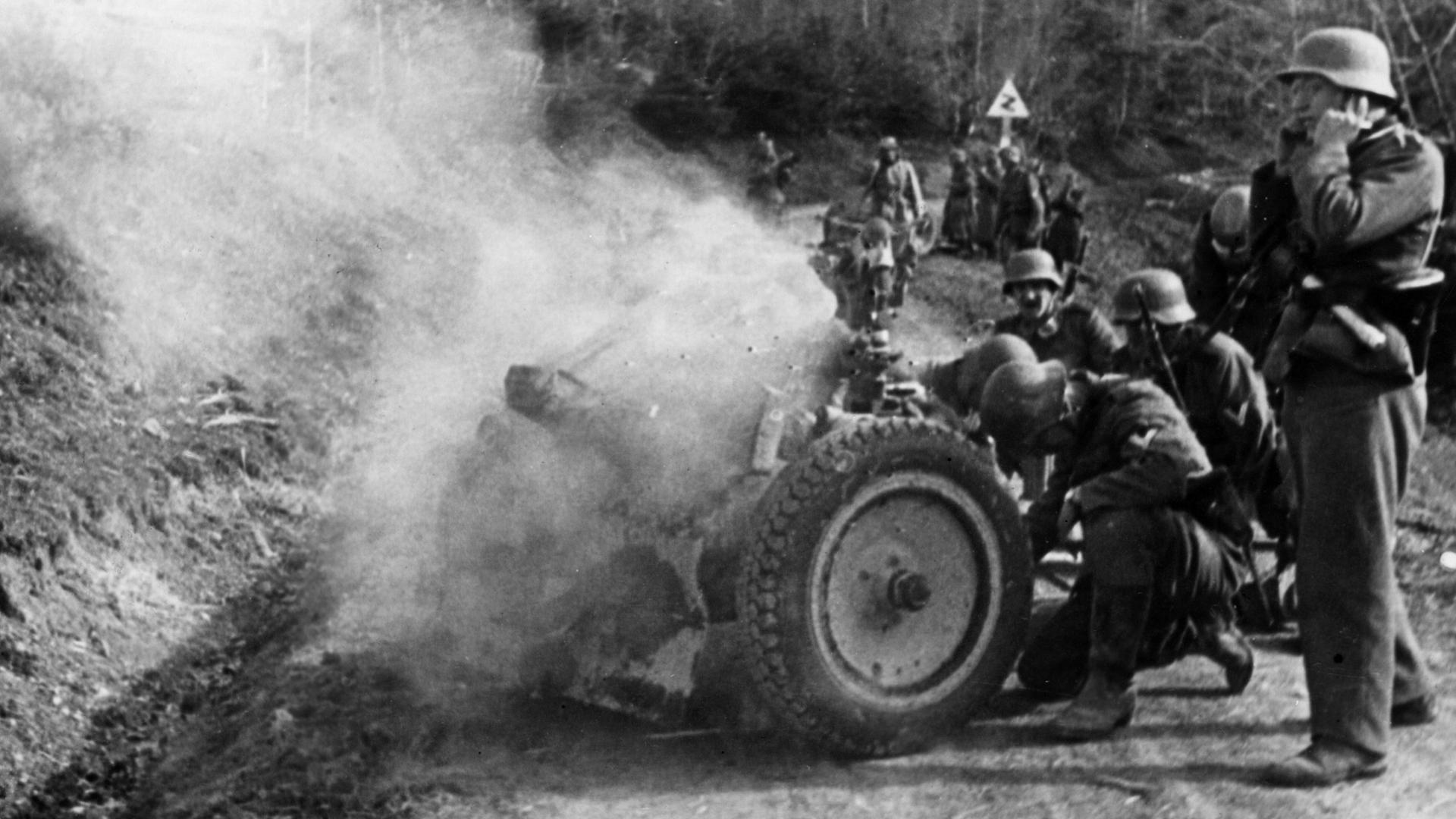 Soldaten der Deutschen Wehrmacht feuern ein Infanteriegeschütz auf einer Passstraße ab.