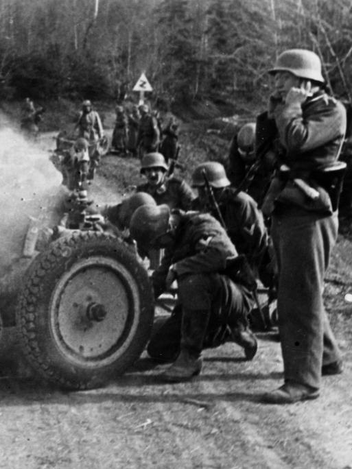 Soldaten der Deutschen Wehrmacht feuern ein Infanteriegeschütz auf einer Passstraße ab.