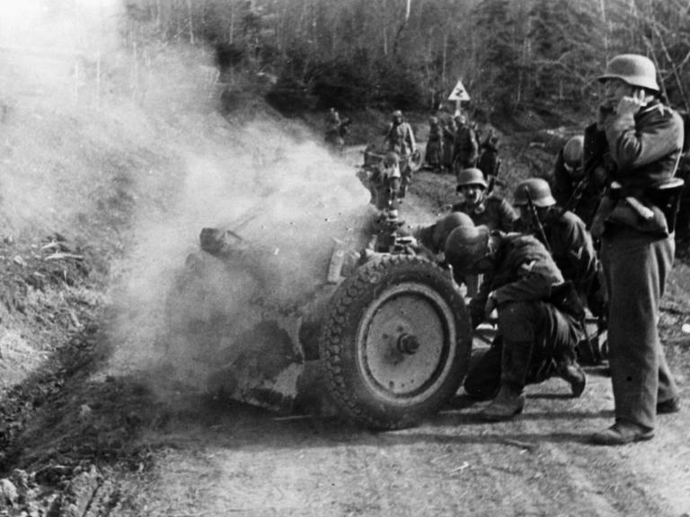 Soldaten der Deutschen Wehrmacht feuern ein Infanteriegeschütz auf einer Passstraße ab.