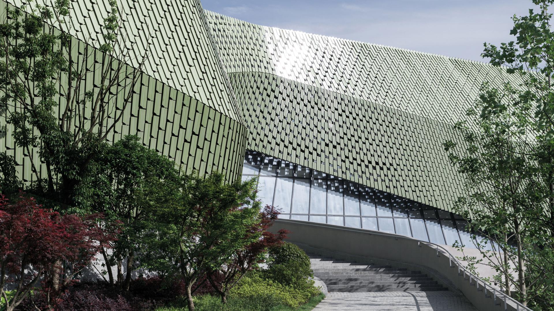 Das städtebauliche Ausstellungszentrum in Ningbo/China, eine Zusammenarbeit mit Schmidhuber München. Zu sehen ist ein grünliches, modern geschwungenes Gebäude. Die Außenhaut erinnert an Reptilienschuppen. 