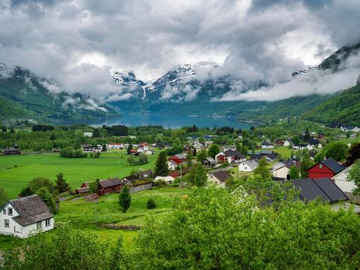 Wolkenverhangenes Bergdorf in Norwegen oberhalb eines Sees am Hange eines Berges.