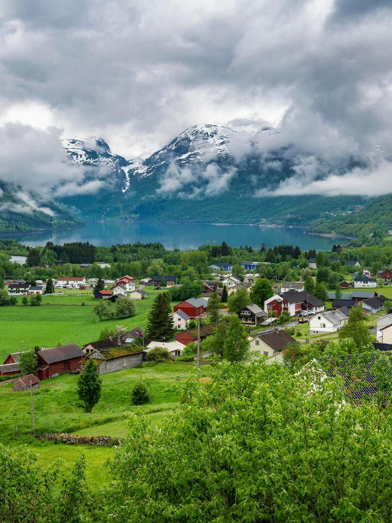 Wolkenverhangenes Bergdorf in Norwegen oberhalb eines Sees am Hange eines Berges.