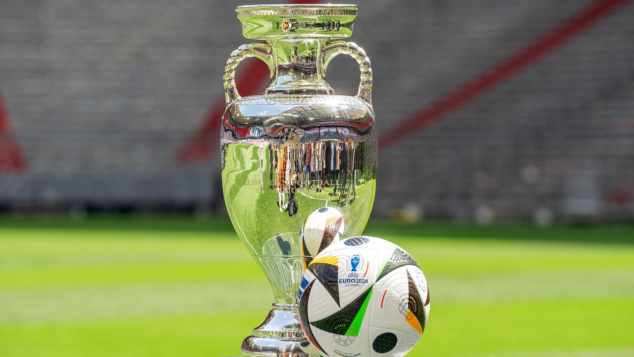 Der Fußball-EM-Pokal steht auf einem Glaspodest, daneben der offizielle Fußball der Euro 2024.