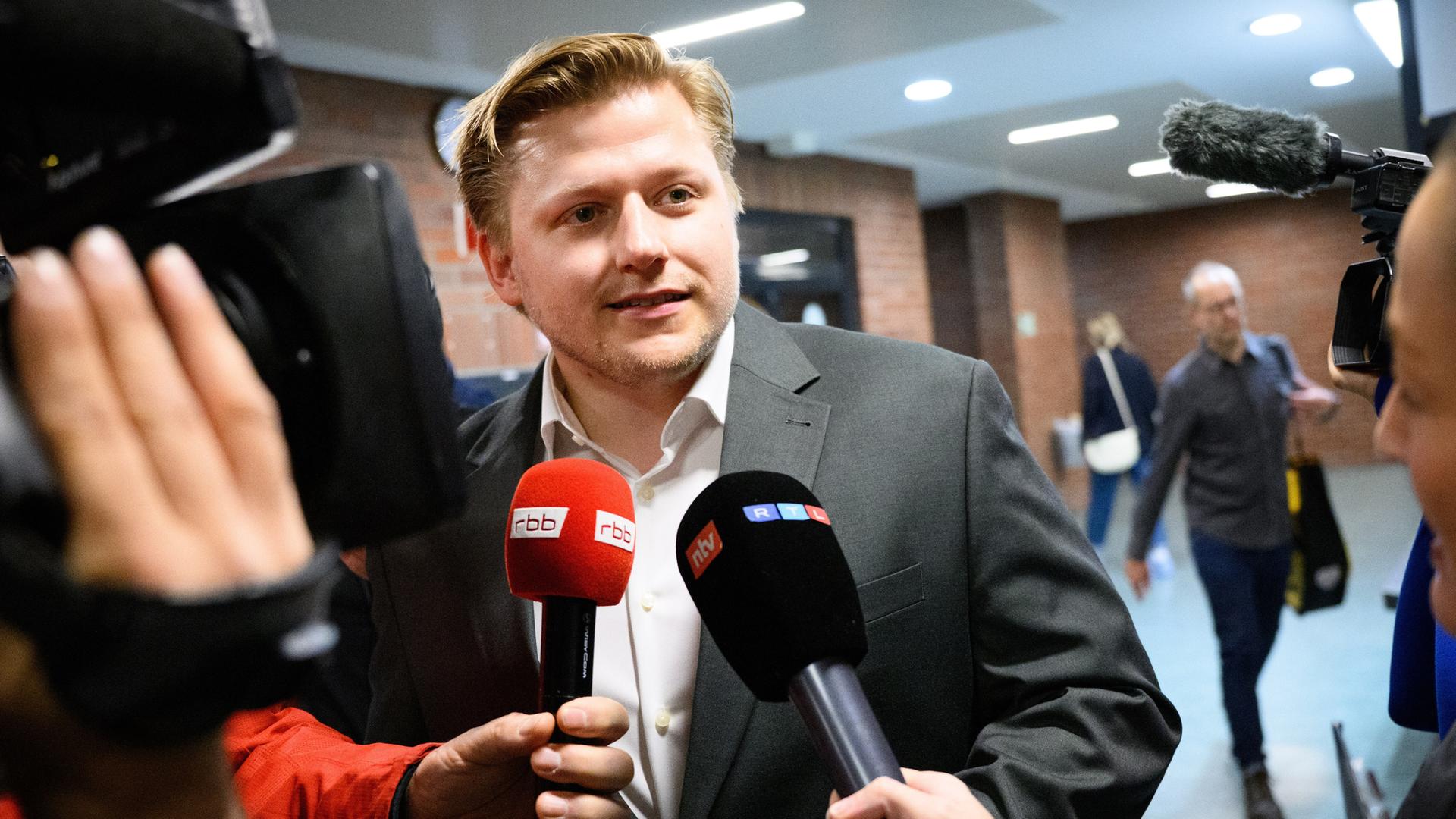 Der Satiriker El Hotzo steht im Flur des Amtsgerichts Tiergarten und gibt Medienvertretern Interviews.