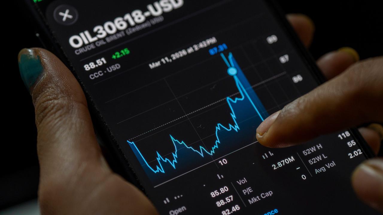 Ein Hand hält ein Mobiltelefon auf dem der Chart des Ölpreises zu sehen ist, der stark angestiegen ist.