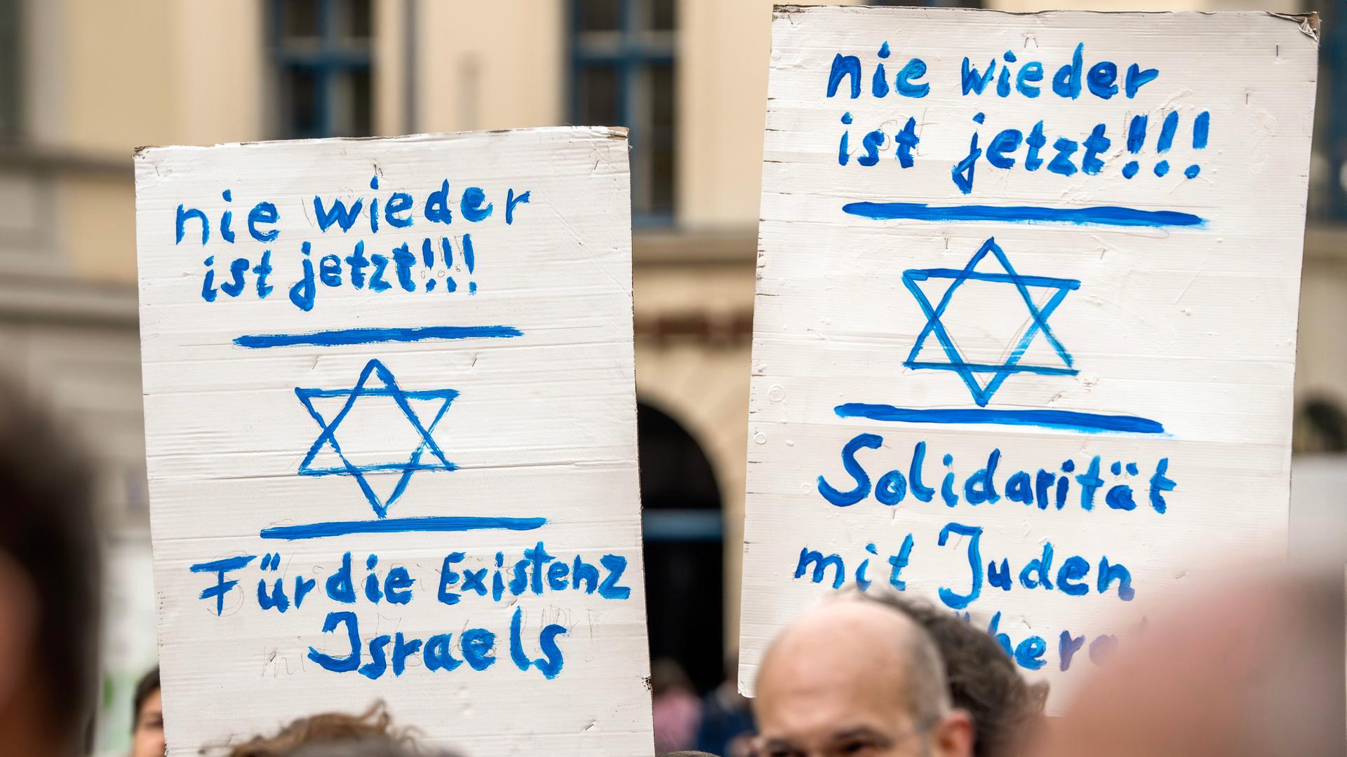 "Nie wieder ist jetzt" steht auf zwei Plakaten, die am 18. Februar 2024 bei einer Kundgebung in München hochgehalten werden